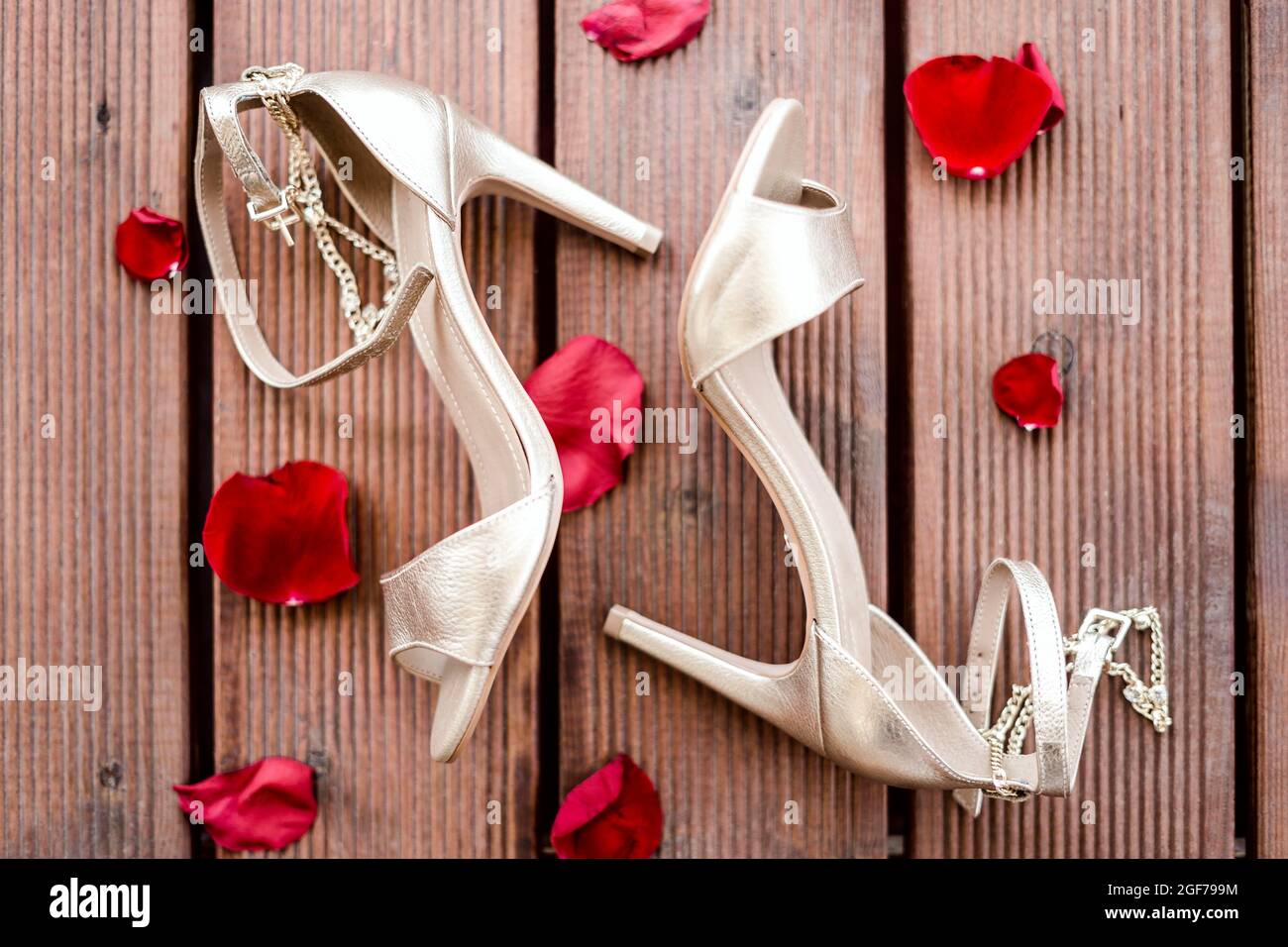 Golden high heel shoes with rose petals on wooden background Stock Photo