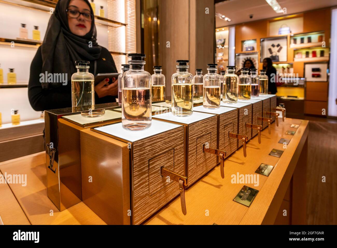 Woman with headscarf looking into lined up perfume bottles, luxury department stores, Harrods, London, England, Great Britain Stock Photo