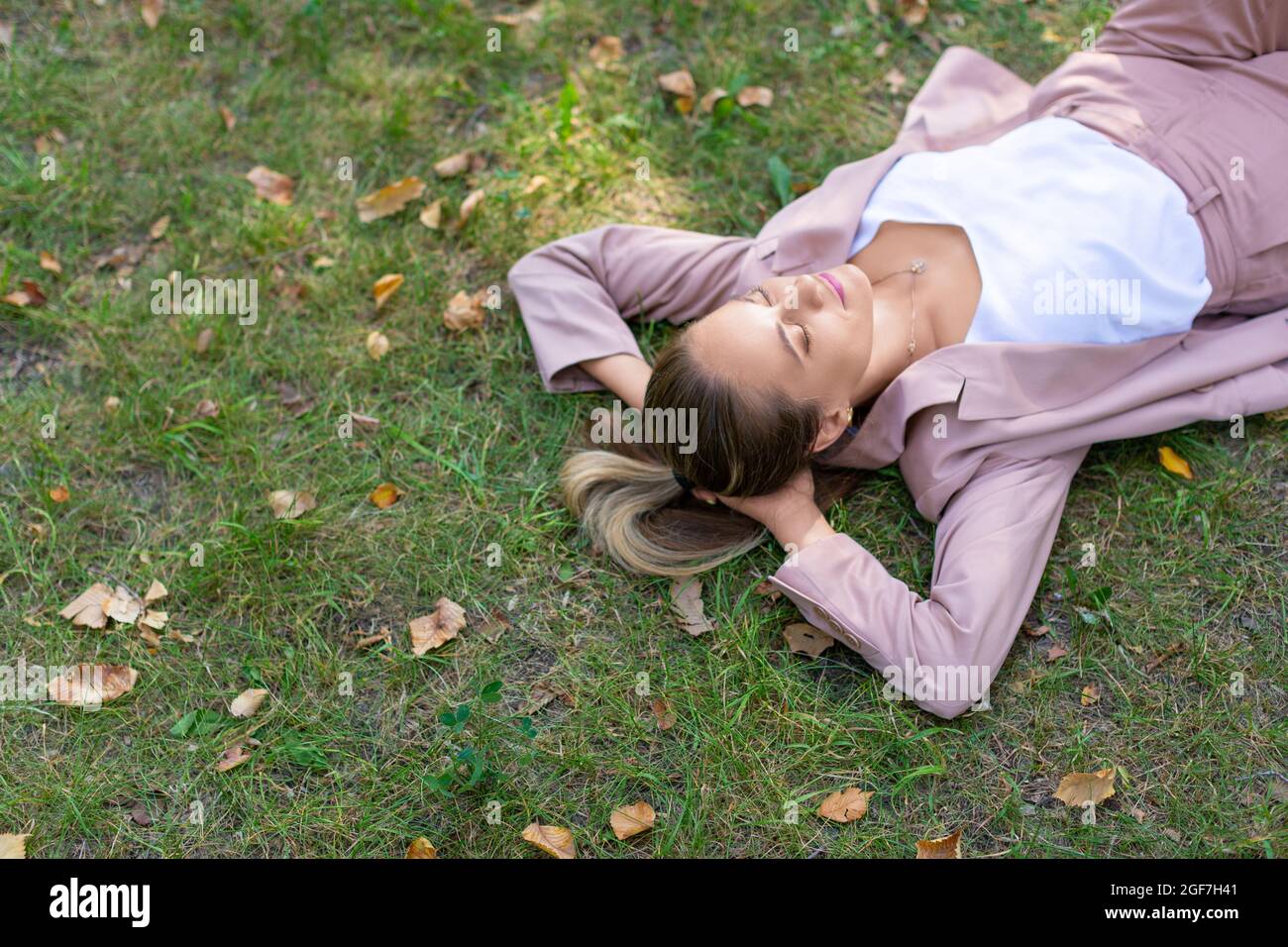 Digital detox concept - pensive young woman lies in the park on the grass with closed eyes. She takes a break from office work. Close-up top view. Stock Photo