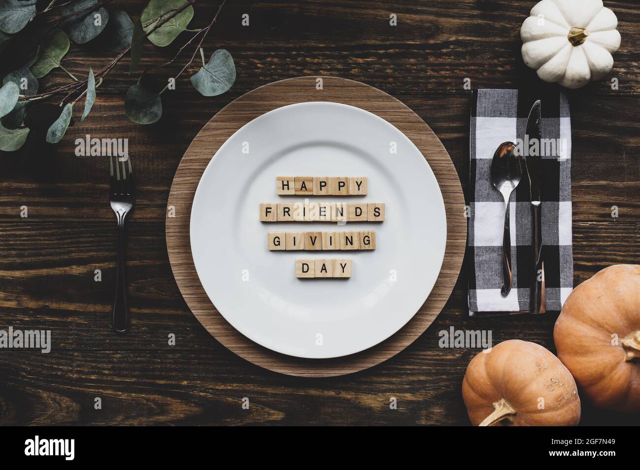 Thanksgiving place setting with plate, napkin, on a  decorated table shot from flat lay or top view position. Happy Friendsgiving Day spelled out with Stock Photo