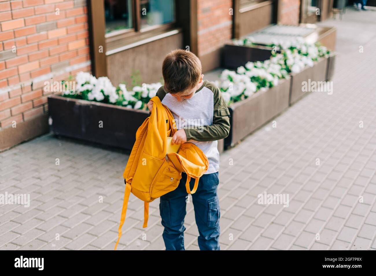 Back to school. Cute child packing backpack, holding notepad and training books going to school. Boy pupil with bag. Elementary school student going Stock Photo