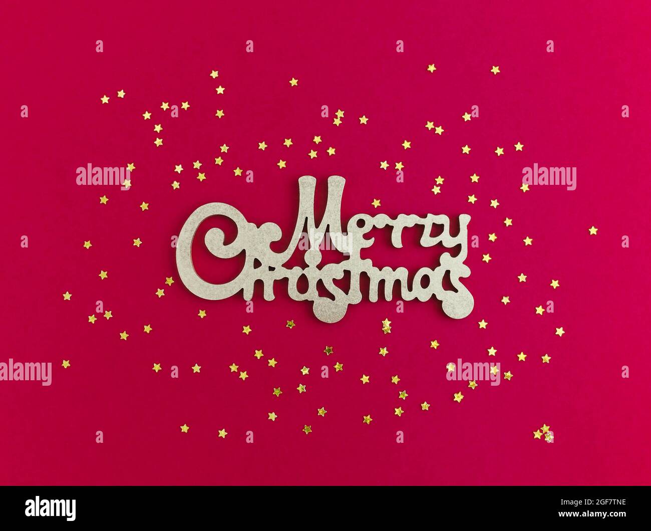Merry Christmas gold greeting message and golden stars confetti on red background. Top view. Bright Christmas greeting card. Stock Photo