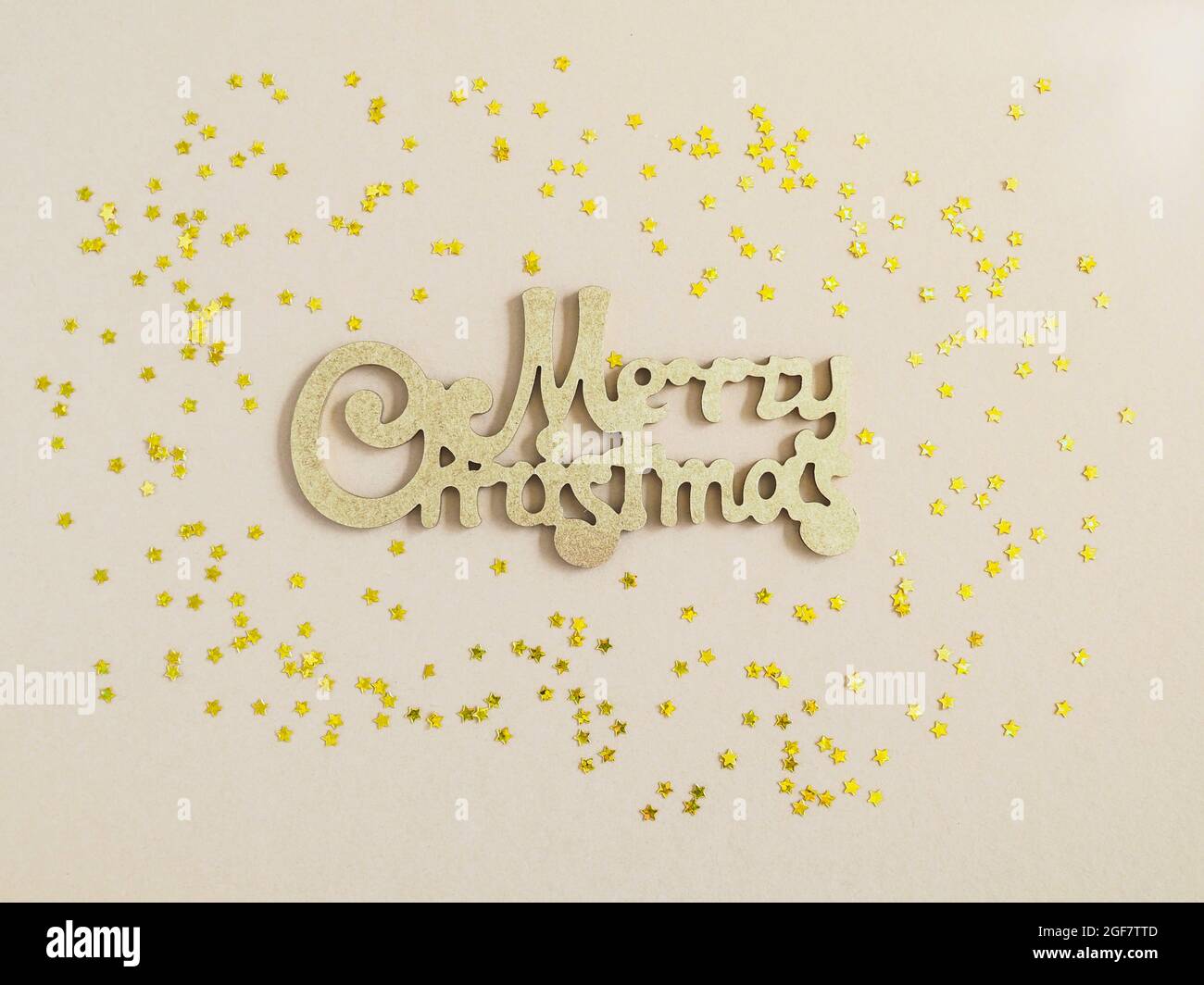 Merry Christmas gold greeting message and golden stars confetti on beige background. Top view. Bright Christmas greeting card. Stock Photo