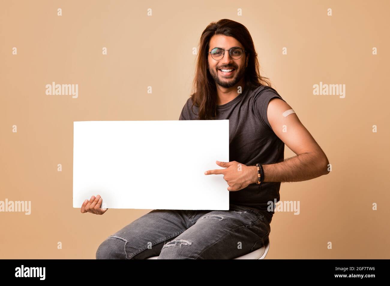 Handsome middle-eastern young man got vaccinated, holding blank board Stock Photo
