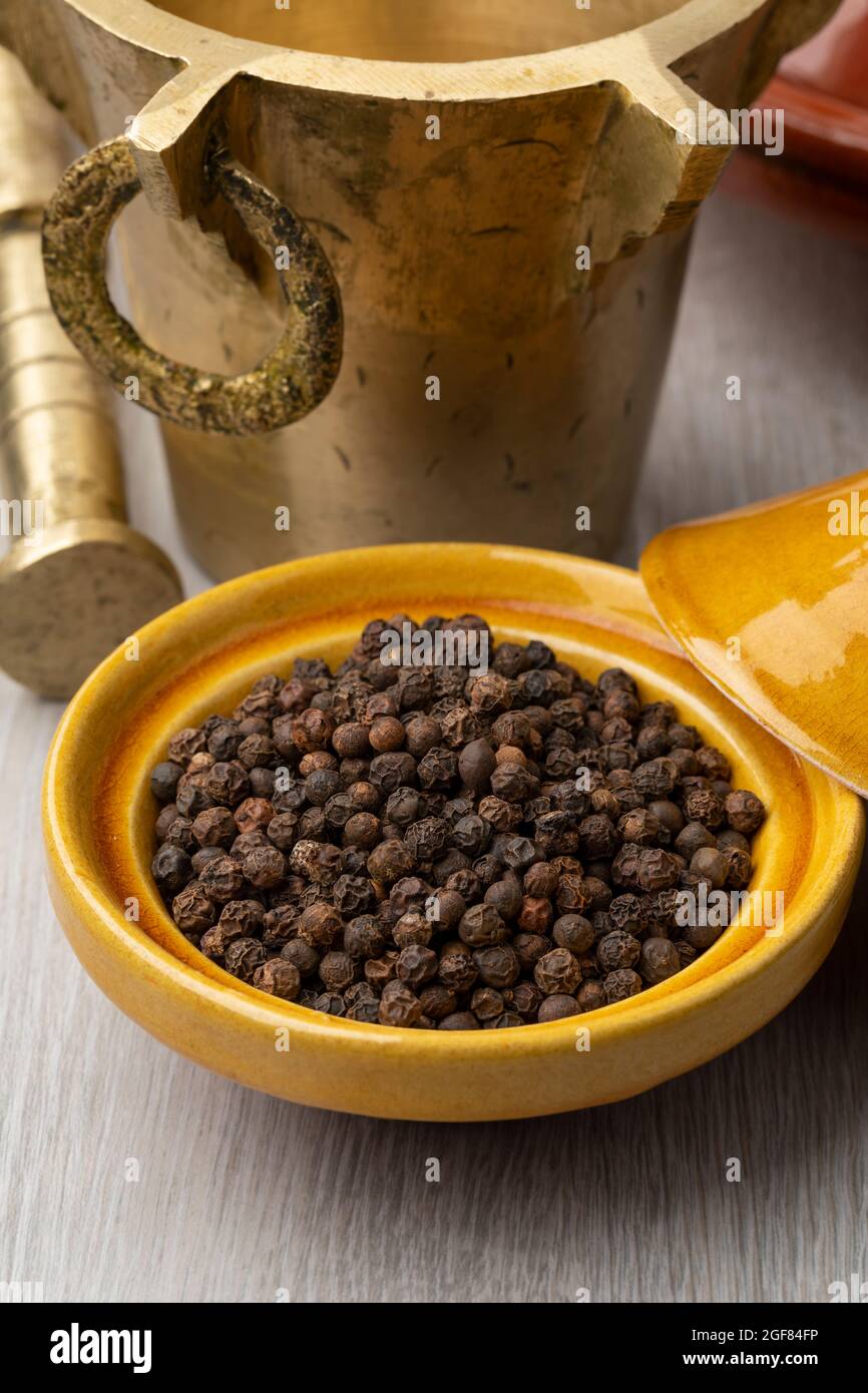 Traditional Moroccan metal Mortar and pestle with a tajine dried  black pepper seeds in front close up Stock Photo
