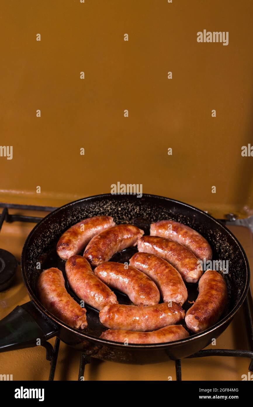 Fried sausages on a kitchen stove, close up on a pan. Fatty and fried foods are a source of cardiovascular disease. Stock Photo