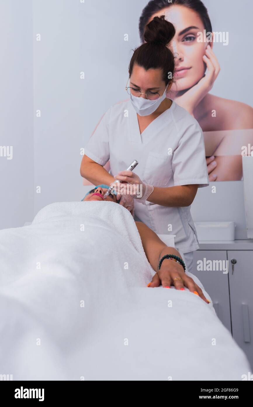 Professional cosmetologist performing procedure of mesotherapy with dermapen to adult woman Stock Photo