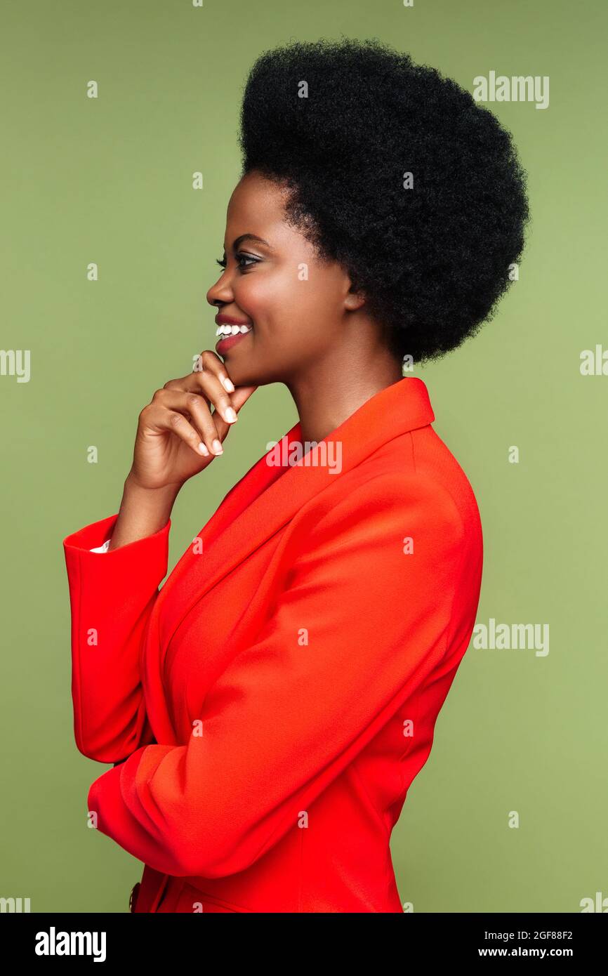 Proud african woman smiling. Profile of successful businesswoman in red suit excited touching chin Stock Photo