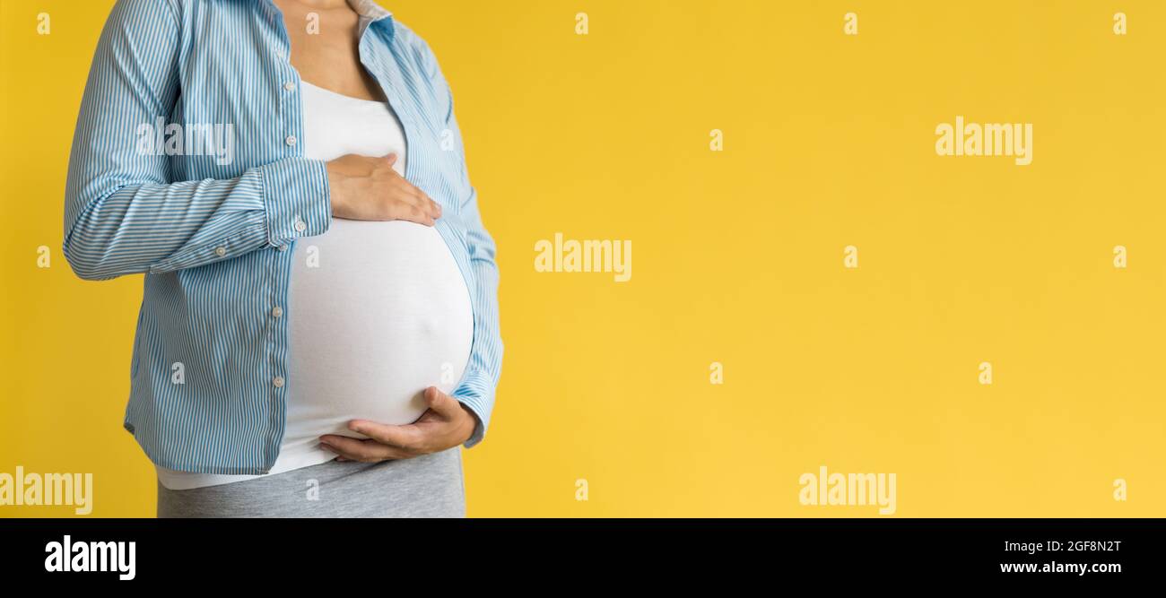 Motherhood, femininity, love, care, waiting, hot summer - bright banner Close-up unrecognizable pregnant woman in shirt with small baby shoes hand Stock Photo