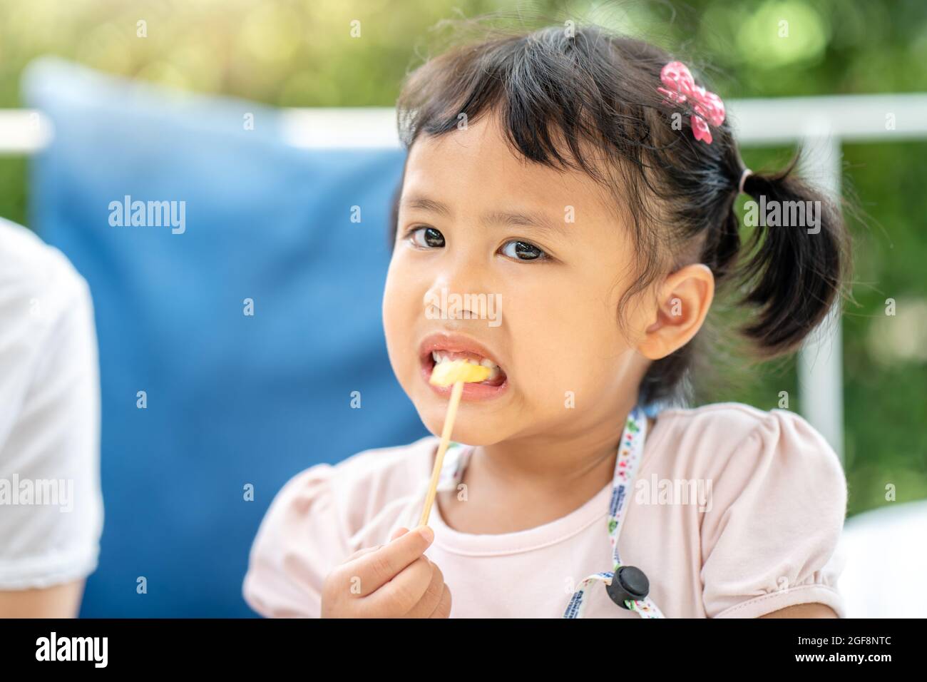 Cute little Asian girl eating a fruit slice on a stick Stock Photo