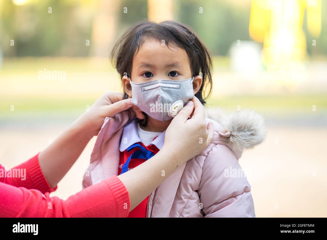 Mother's hands helping her daughter wear face mask going to school