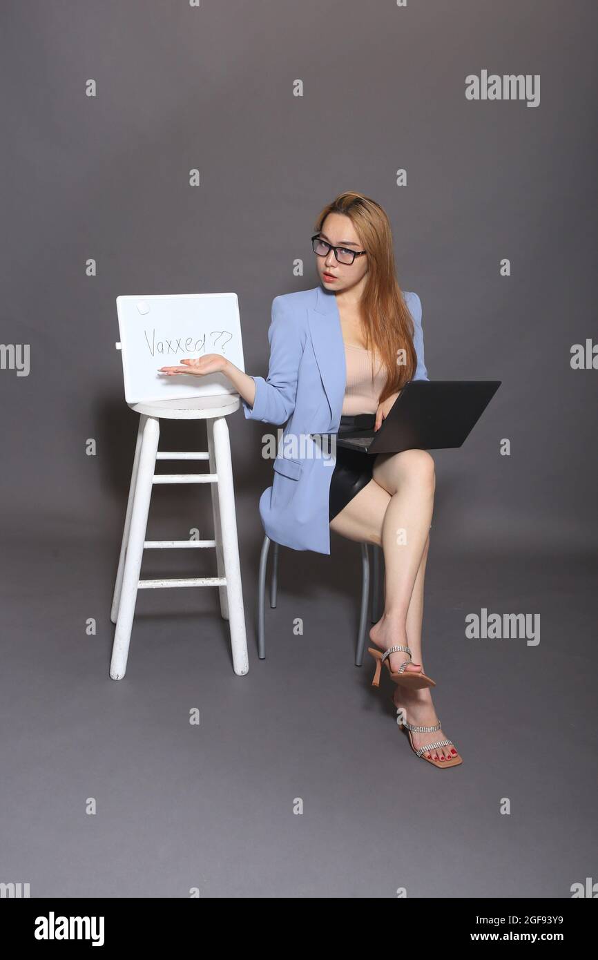 vertical image of business woman sitting down with a computer on her lap while she points to a vaccination sign Stock Photo