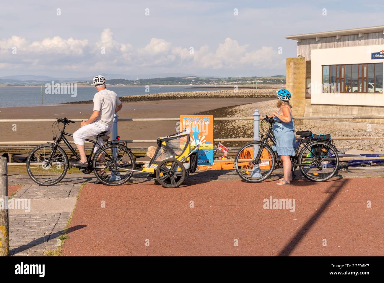 Mature cyclist couple with luxury doggy trailer carrying two happy terrier dogs at the seafront in Morecambe, UK. Stock Photo