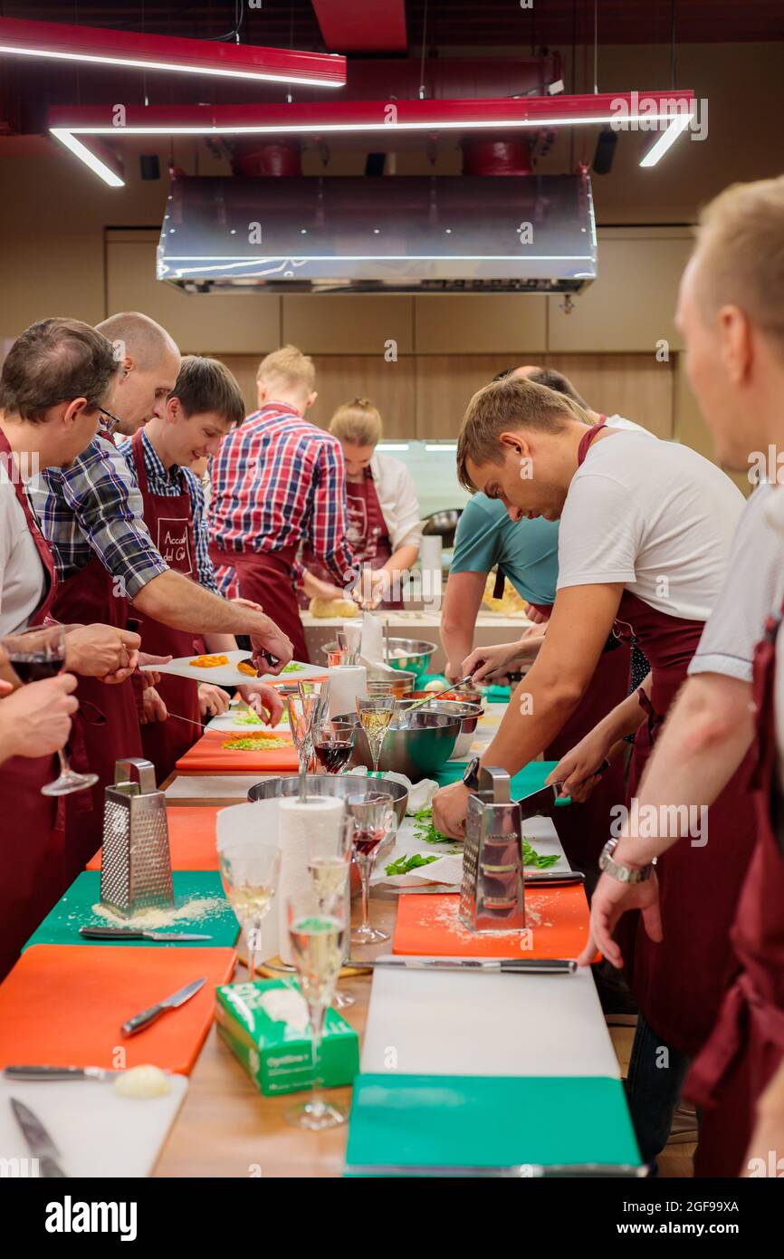 A group of colleagues celebrate a corporate lunch by cooking together. A community of people prepares lunch together in a large kitchen. Moscow, Russi Stock Photo