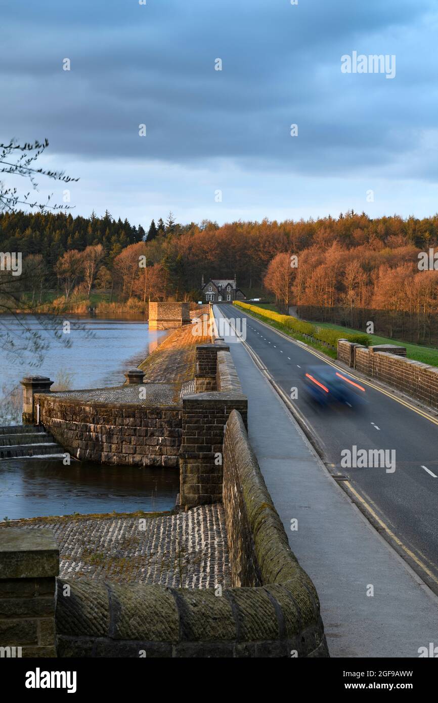 Embankment wall, car lights on road, forest trees, autumn colours, grey evening clouds - Fewston Reservoir, Washburn Valley, Yorkshire, England, UK. Stock Photo