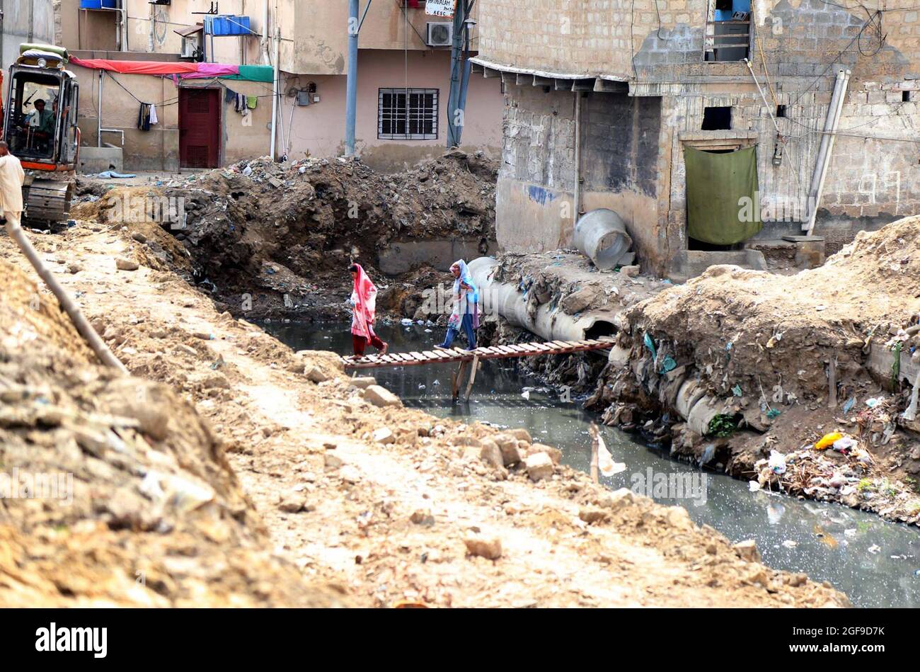 Commuters pass through a wooden bridge on an open drain that may cause a life risk for their showing negligence of concerned authorities, located on Chanesar Goth area of Karachi on Tuesday, August 24, 2021. Stock Photo