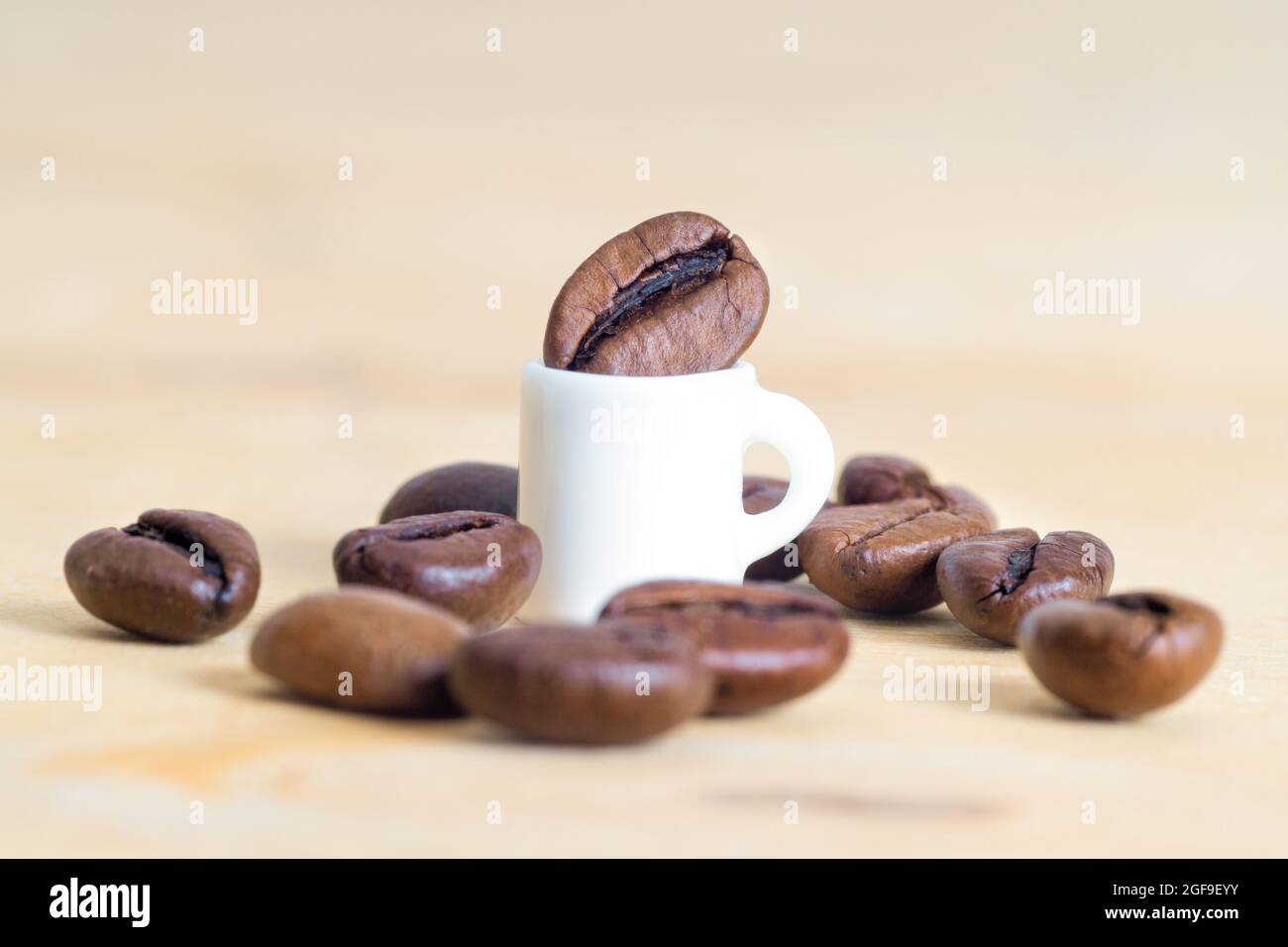 Tiny coffee cup surrounded by scattered coffee beans on a light brown
