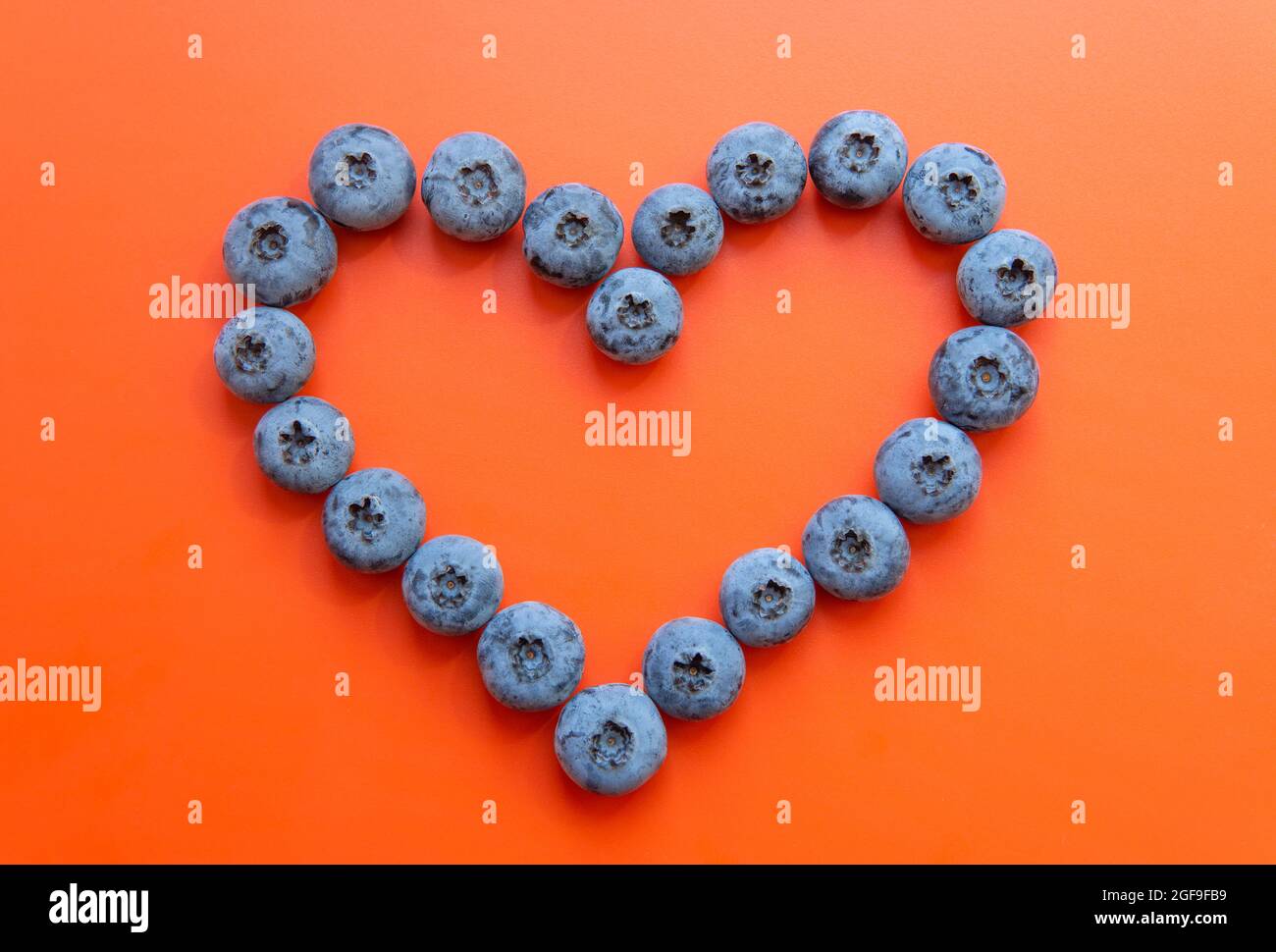 Heart shape made from blueberries on a red background. Heart disease prevention concept. Stock Photo