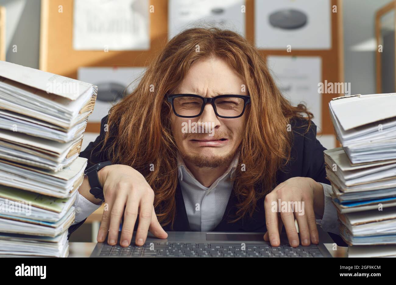 Funny unhappy office worker sitting at desk and crying stressed by huge workload Stock Photo
