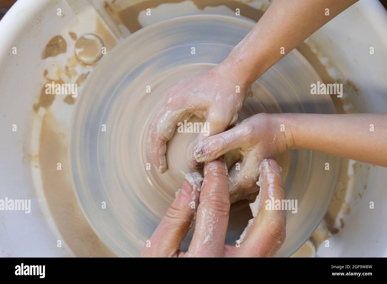 Closeup of a potter's hands and a child's hand with an item on a