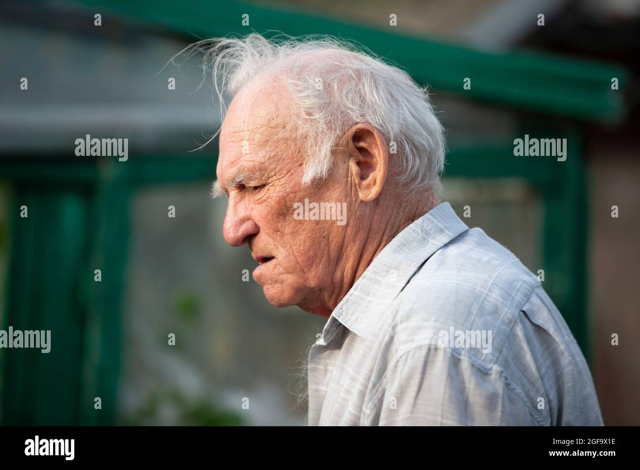 An old gray-haired man with a concerned face and wrinkles in profile. Stock Photo