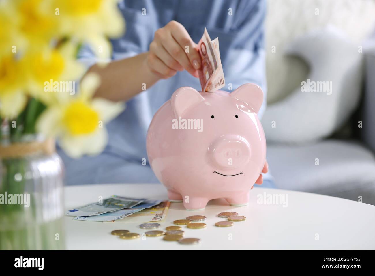 Female hand putting money into piggy bank closeup Stock Photo - Alamy