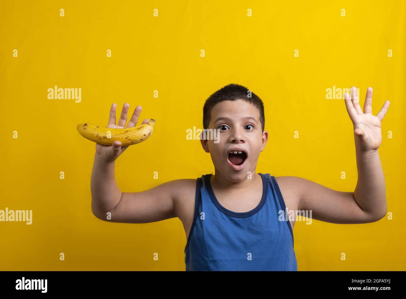 Amazed Hispanic boy with a banana in hand isolated on a yellow background Stock Photo