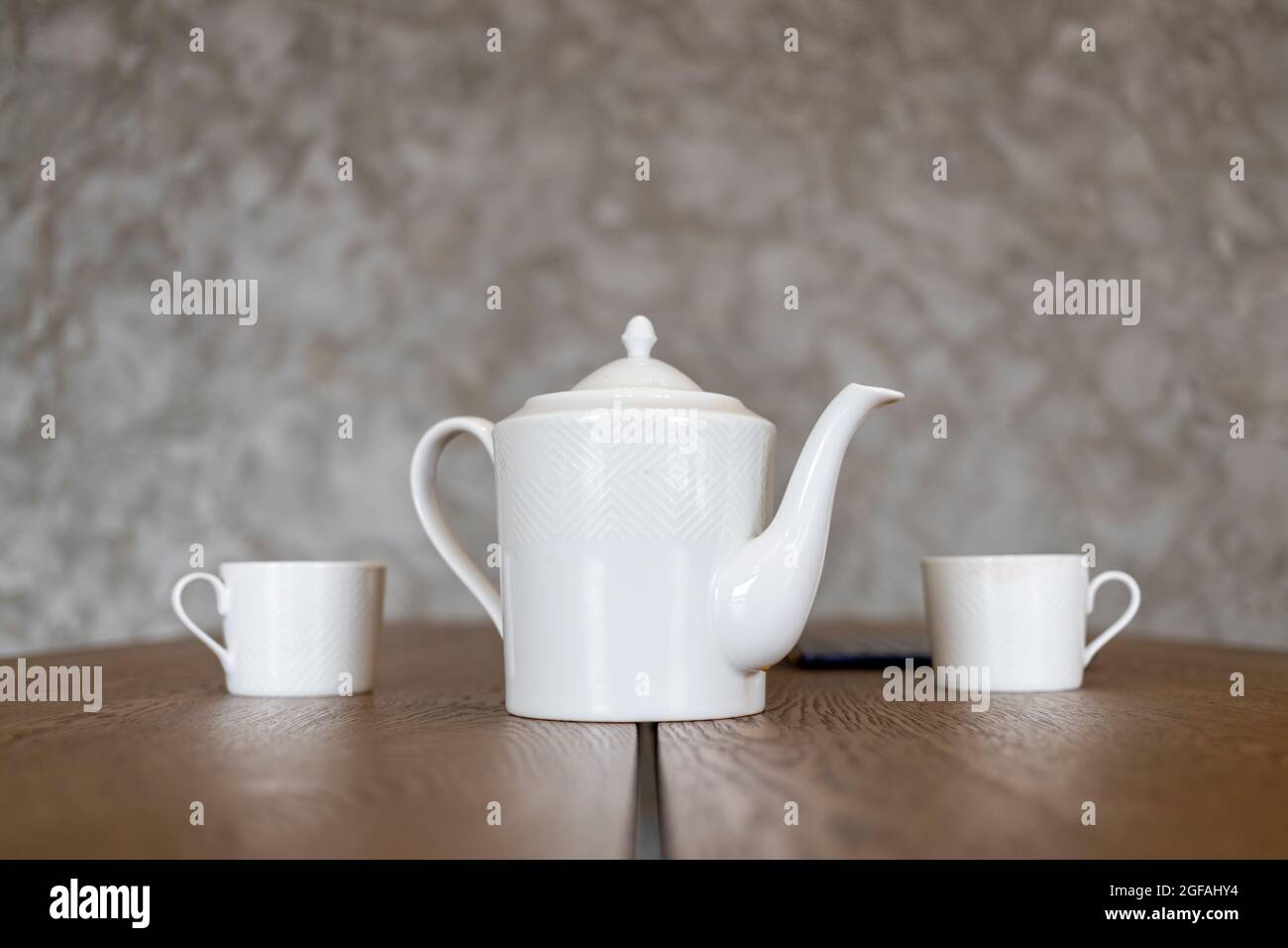 white tea set teapot and two cups stand on a brown table Stock Photo