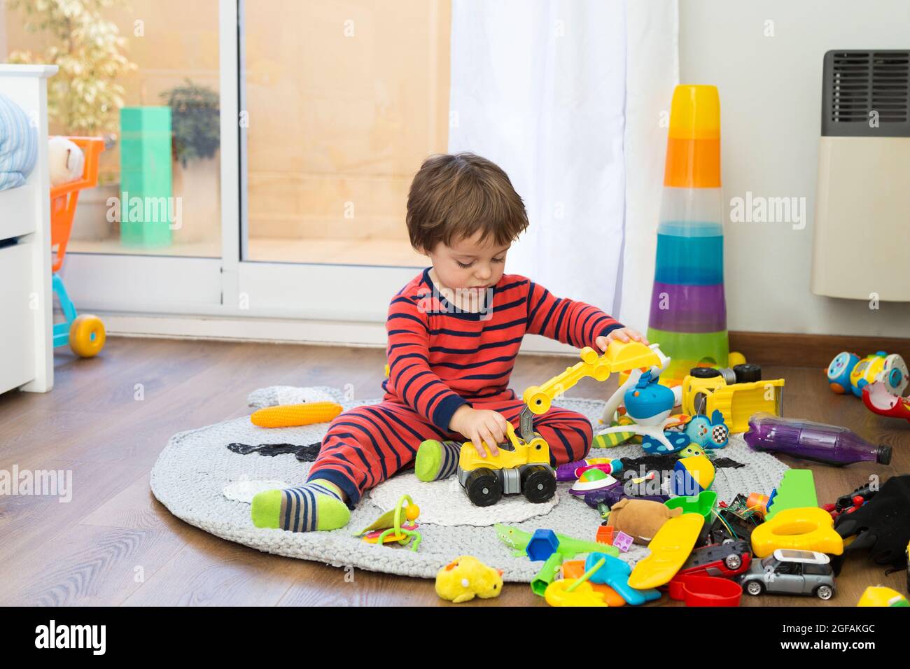 Little toddler playing lonely with many toys in his bedroom. Stock Photo