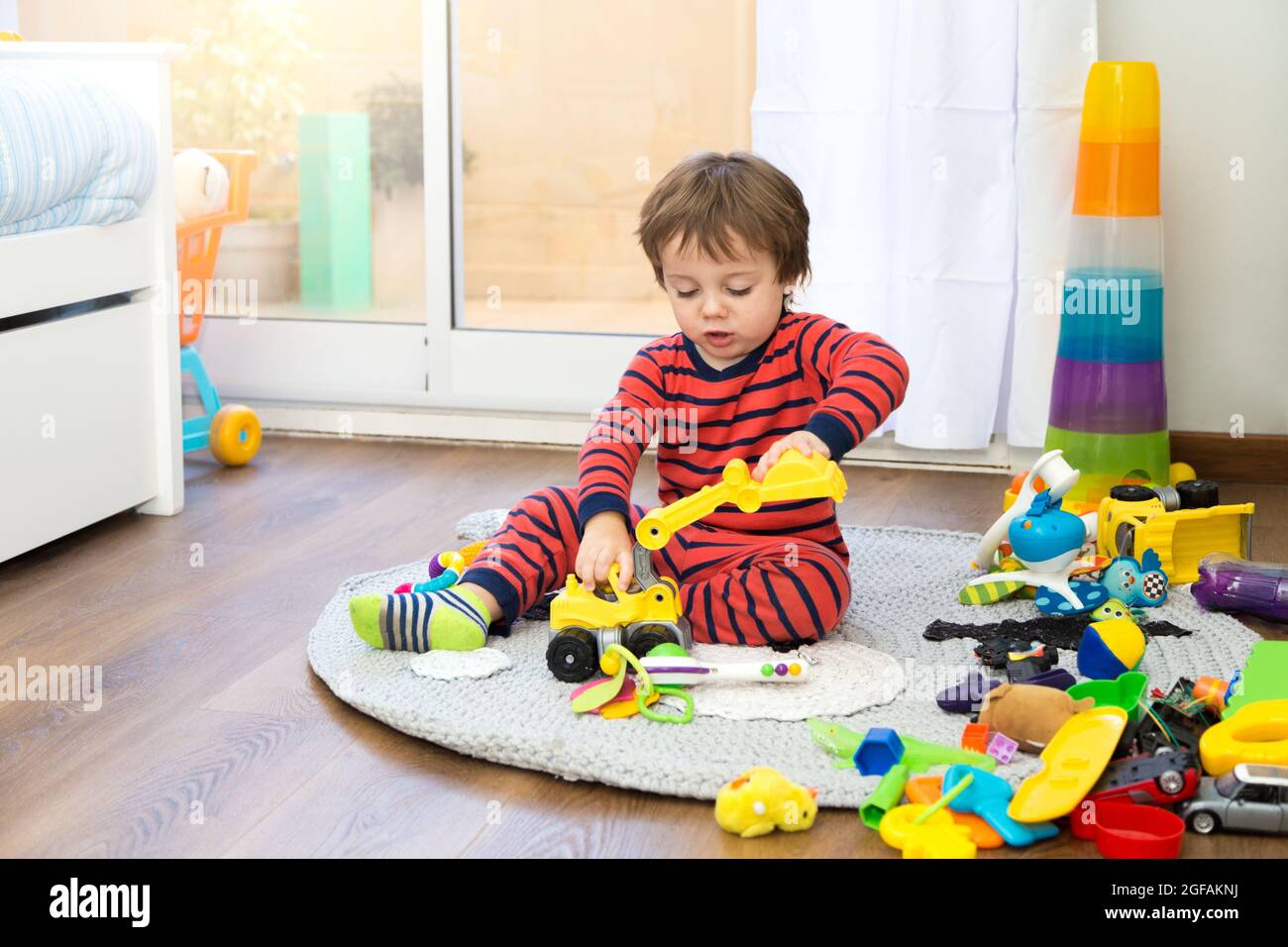Little toddler playing lonely with many toys in his bedroom. Stock Photo