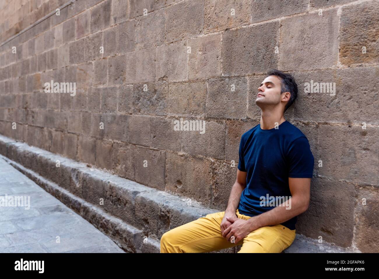 Young latin thoughtful man sitting against a wall outdoors Stock Photo