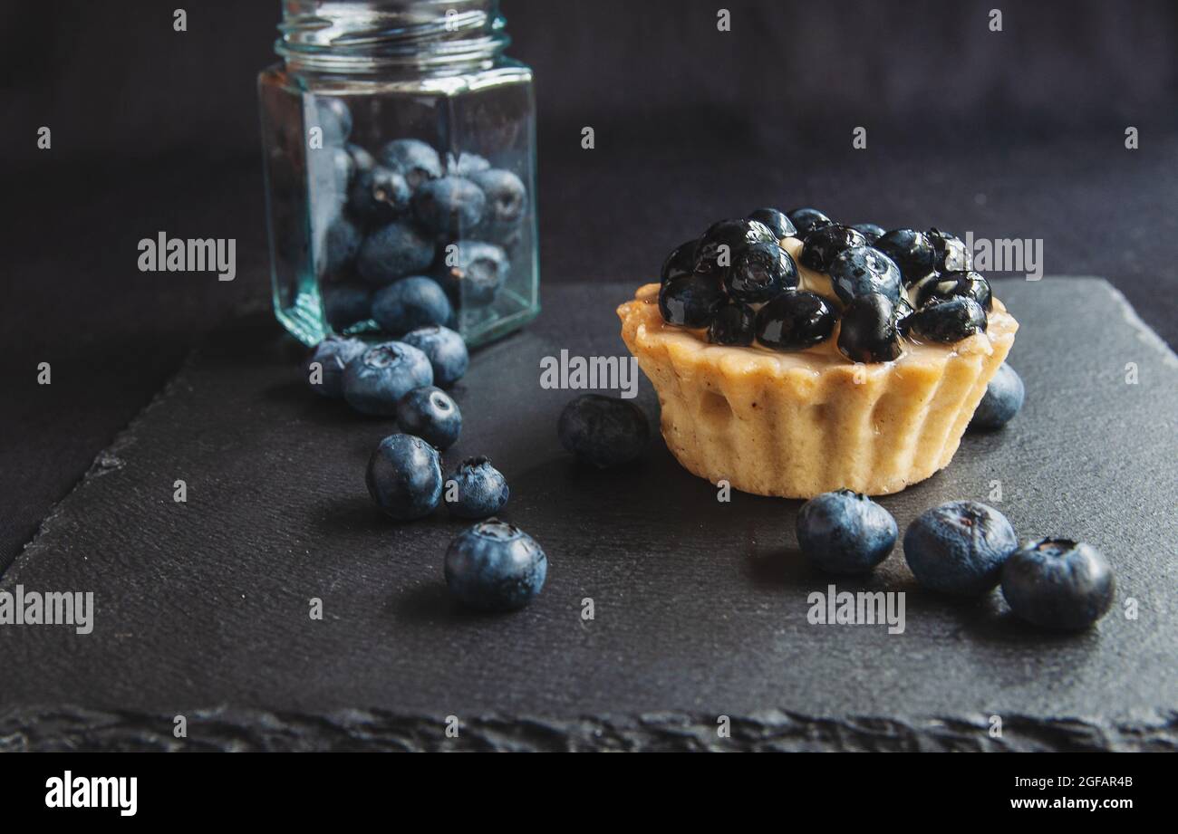 Blueberry tart on a dark background. Blueberry cupcake on black serving board with scattered berries Stock Photo