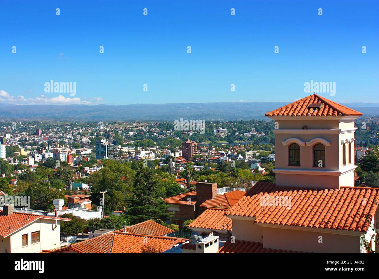 Panoramic view from the top of a hill of the landscape of Carlos Paz Town in a sunny day. A house with red roof in foreground. Stock Photo