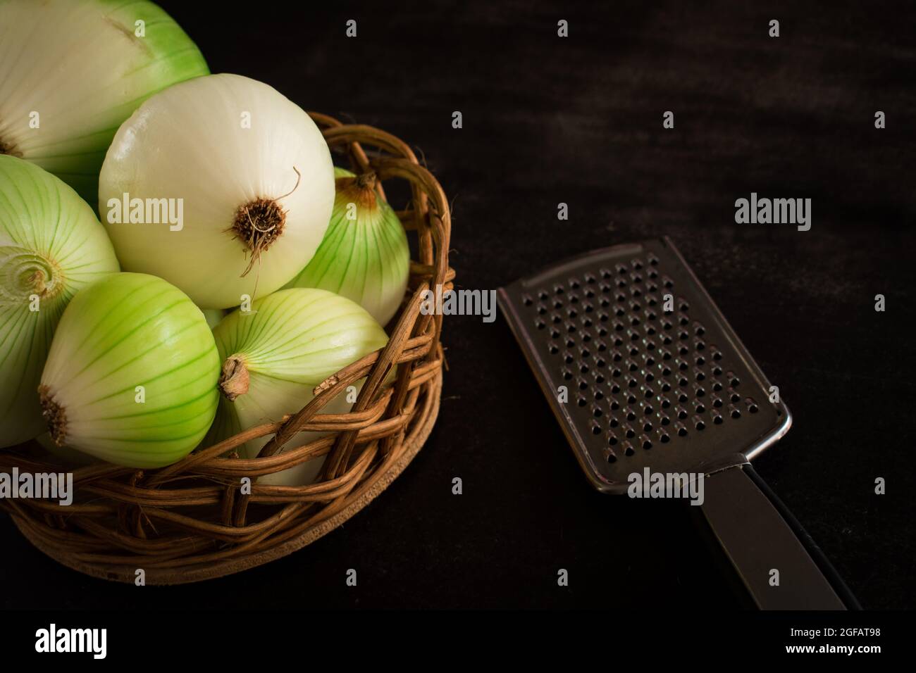 Some big green onions to cook in a brown basket and a metal grater on a black table with copy space Stock Photo