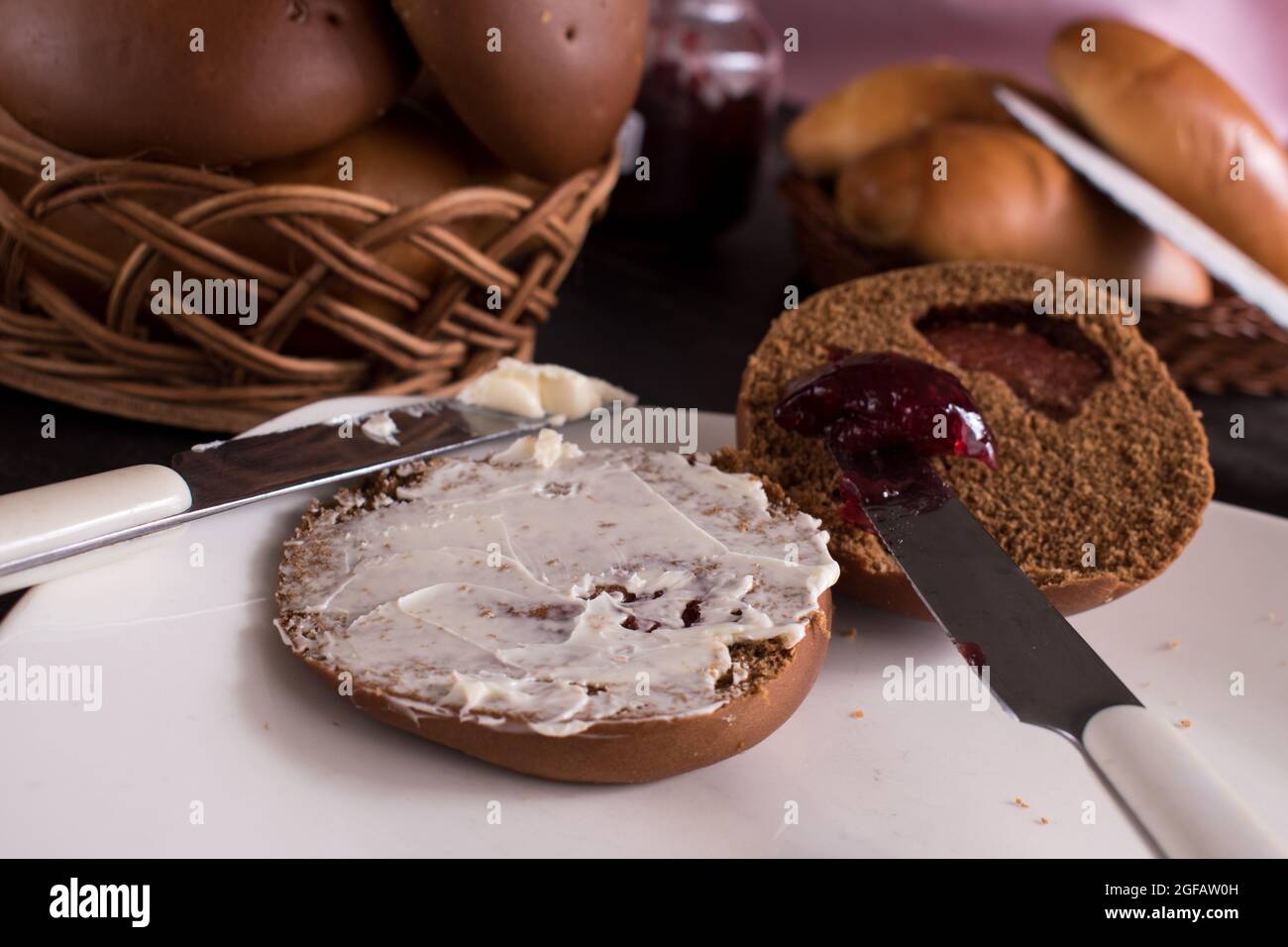 Round brown bread with white butter and  blackberry jam on a white plate with some breads in a bascket at background Stock Photo