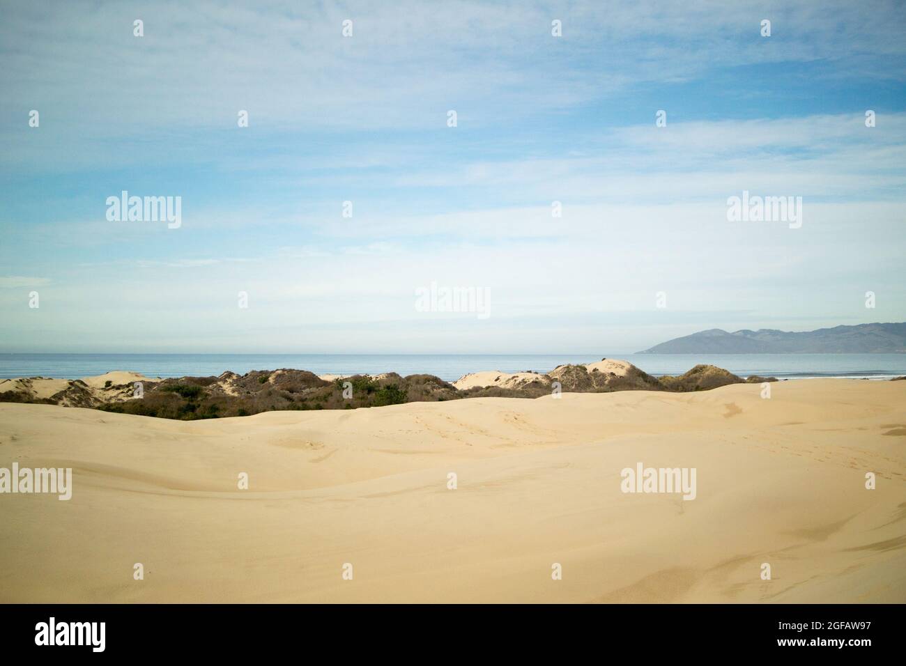 Sand dunes leading to Pacific Ocean on cloudy winter's day, with hazy gray mountains on the horizon Stock Photo