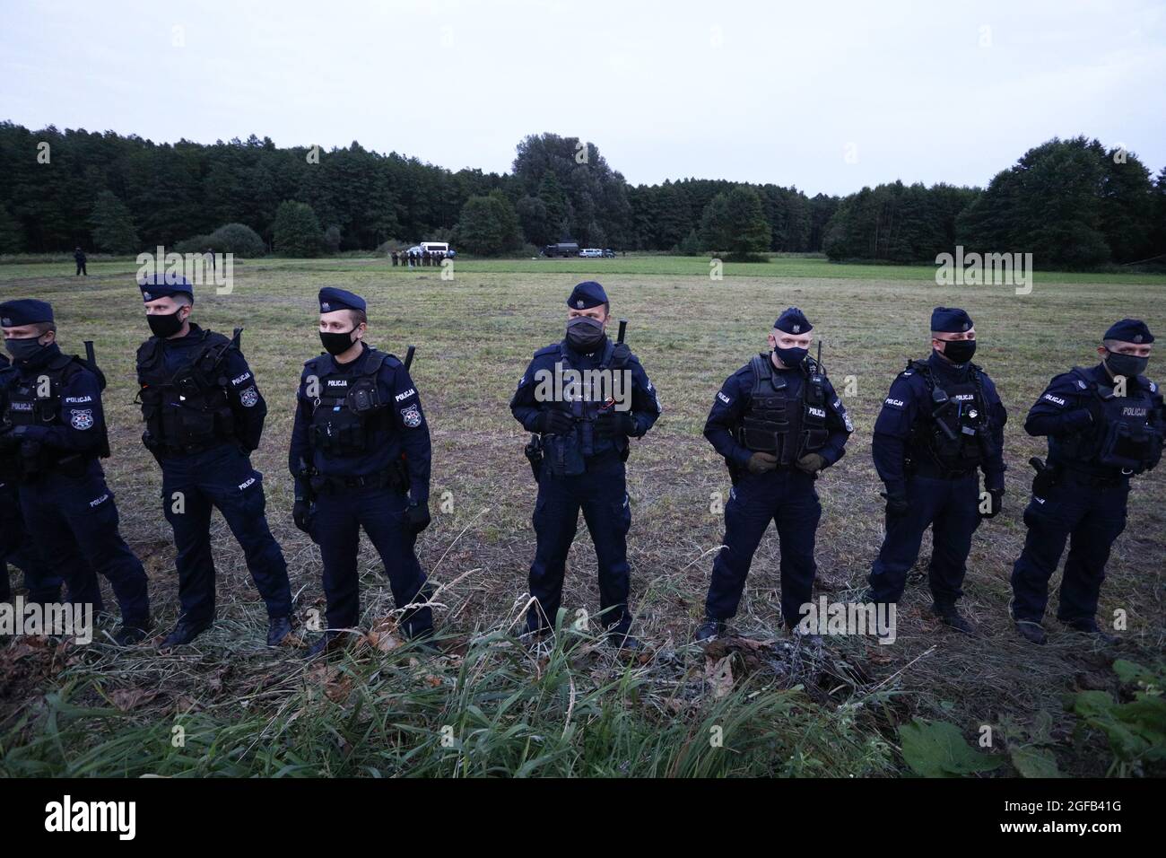 Police are seen cordonning off an area by a distance of some 300 meters where a group of Afghan refugees is stuck on the Belarusian border in Usnarz Gorny, Poland on August 24, 2021. For 16 days in a row 32 Afghan refugees have been stuck at the Polsh-Belarusian border without food or shelter. Polish authorities deny the migrants have ever reached Polish soil contraty to reports from local individuals who have stated the group has been pushed back by border guards. In August of this year nearly 3000 refugees have been reported attempting to cross the border compred to less than 100 in all of 2 Stock Photo