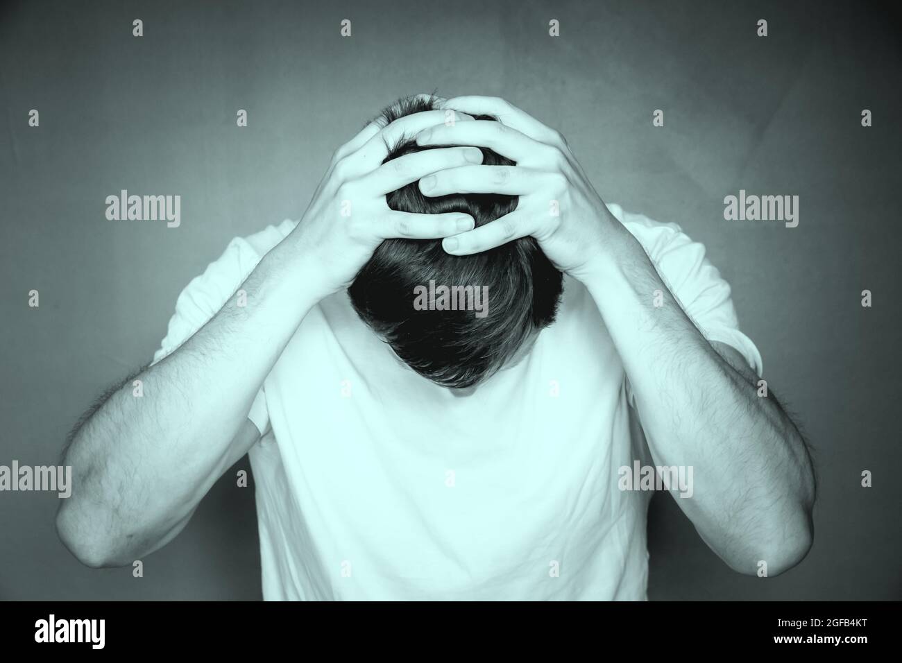 Grayscale shot of a man holding his head with his hands, feeling ...