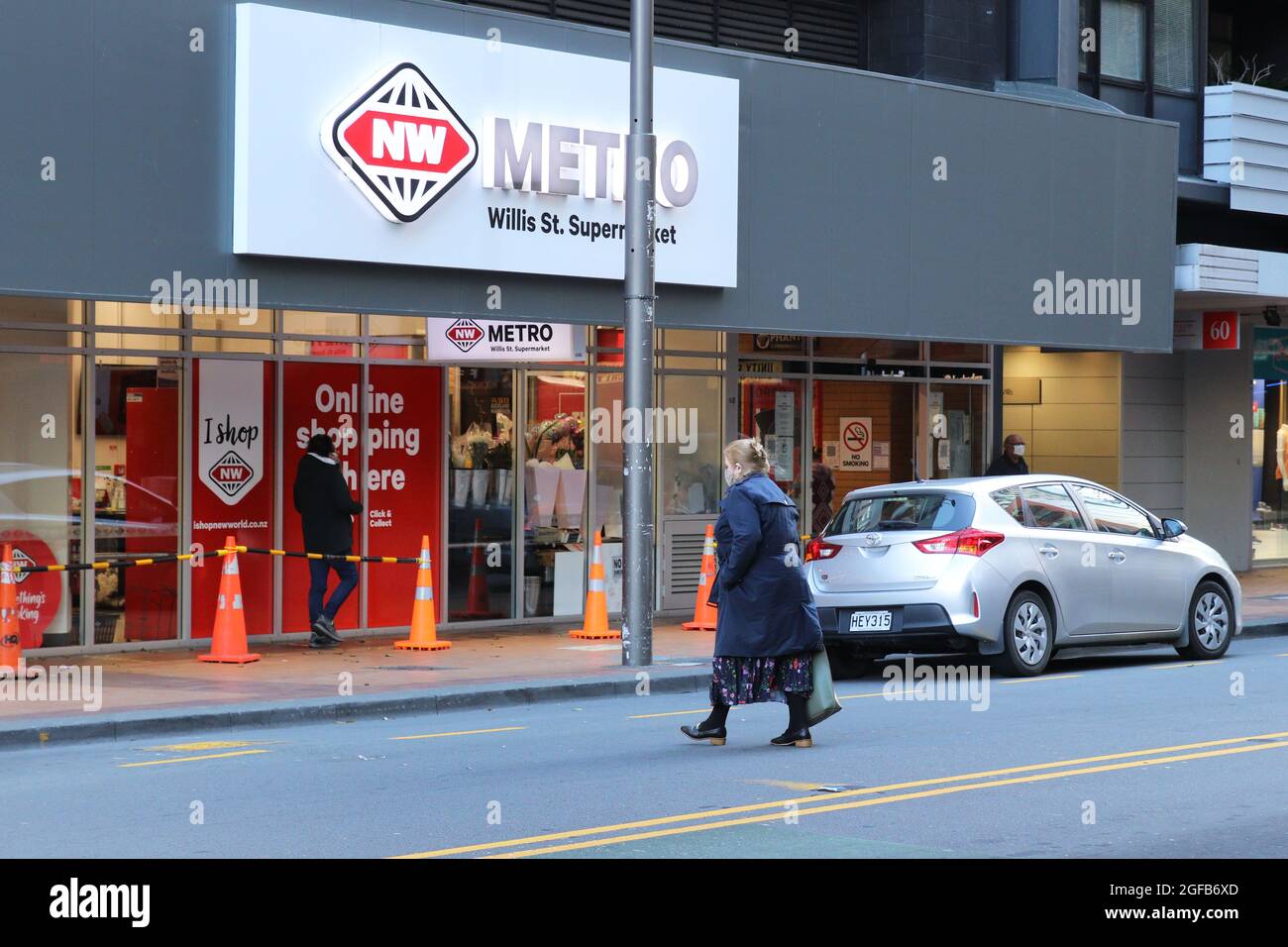 Wellington, New Zealand, 25 August 2021. A woman in a face mask crosses the road towards a supermarket in central Wellington, New Zealand, where only essential shops (such as supermarkets and pharmacies) are allowed to open during a strict Level 4 lockdownn due to a Covid-9 delta variant outbreak. Credit: Lynn Grieveson/Alamy Live News Stock Photo