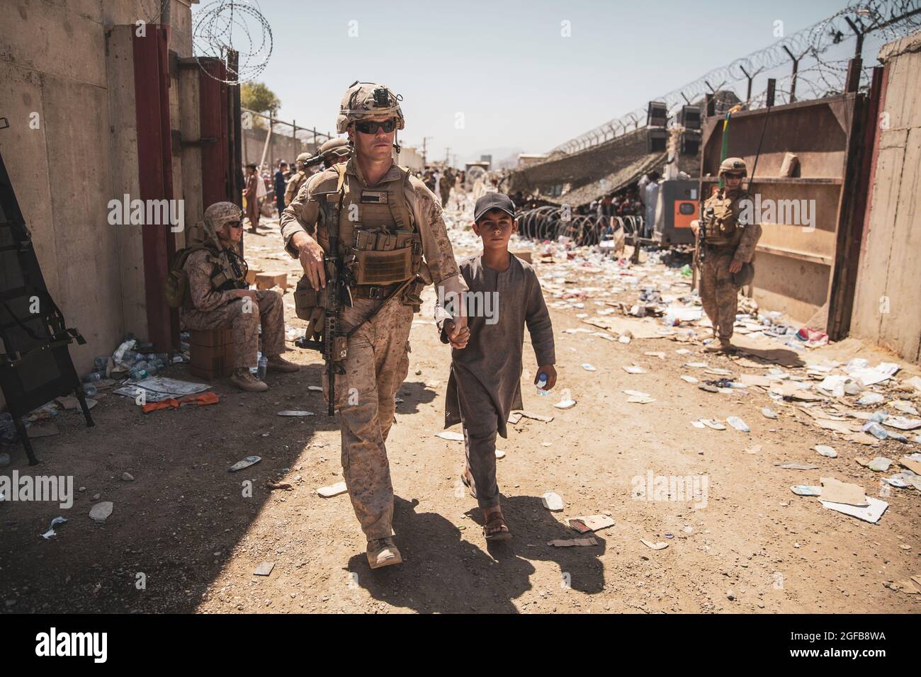 A U.S. Marine with the Special Purpose Marine Air-Ground Task Force-Crisis Response-Central Command (SPMAGTF-CR-CC) escorts a kid to his family during an evacuation at Hamid Karzai International Airport, Kabul, Afghanistan, Aug. 24. U.S. service members and coalition forces are assisting the Department of State with a non-combatant evacuation operation (NEO) in Afghanistan. (U.S. Marine Corps photo by Staff Sgt. Victor Mancilla) Stock Photo