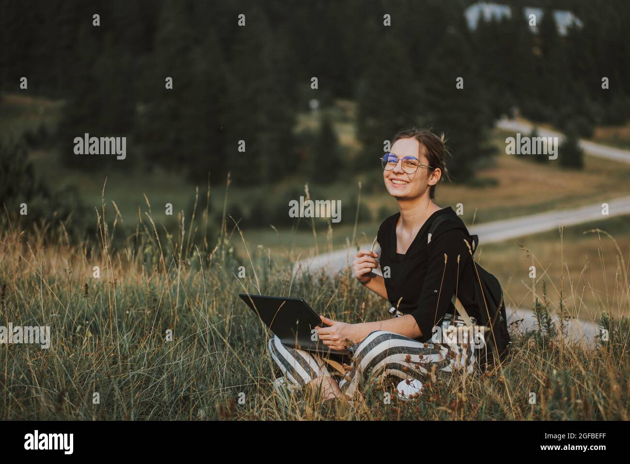 happy woman freelancer with glasses working on laptop, remote location in nature Stock Photo