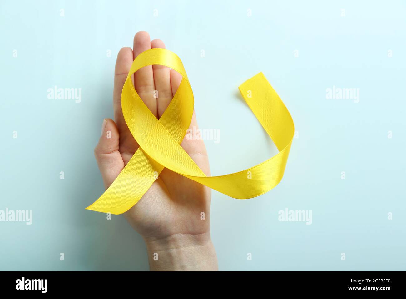 Hand holding yellow ribbon on light grey background Stock Photo - Alamy