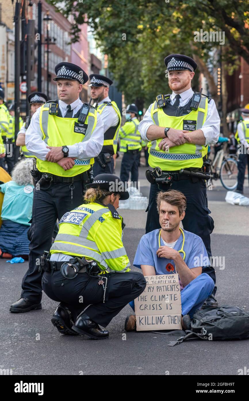 London, UK. 24th Aug, 2021. Police talk to a protester who has sat in superglue to block the road at Cambridge Circus, during the demonstration.‘The Impossible Rebellion' protest against climate change, global warming, which plans to target the root cause of the climate and ecological crisis and to demand the government divest from fossil fuel companies by Extinction Rebellion. (Photo by Dave Rushen/SOPA Images/Sipa USA) Credit: Sipa USA/Alamy Live News Stock Photo