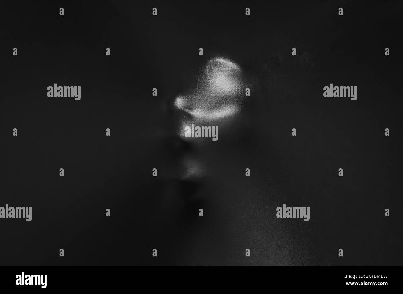 Screaming human face pressing through black fabric with shine and dark side for Halloween background concept. Stock Photo