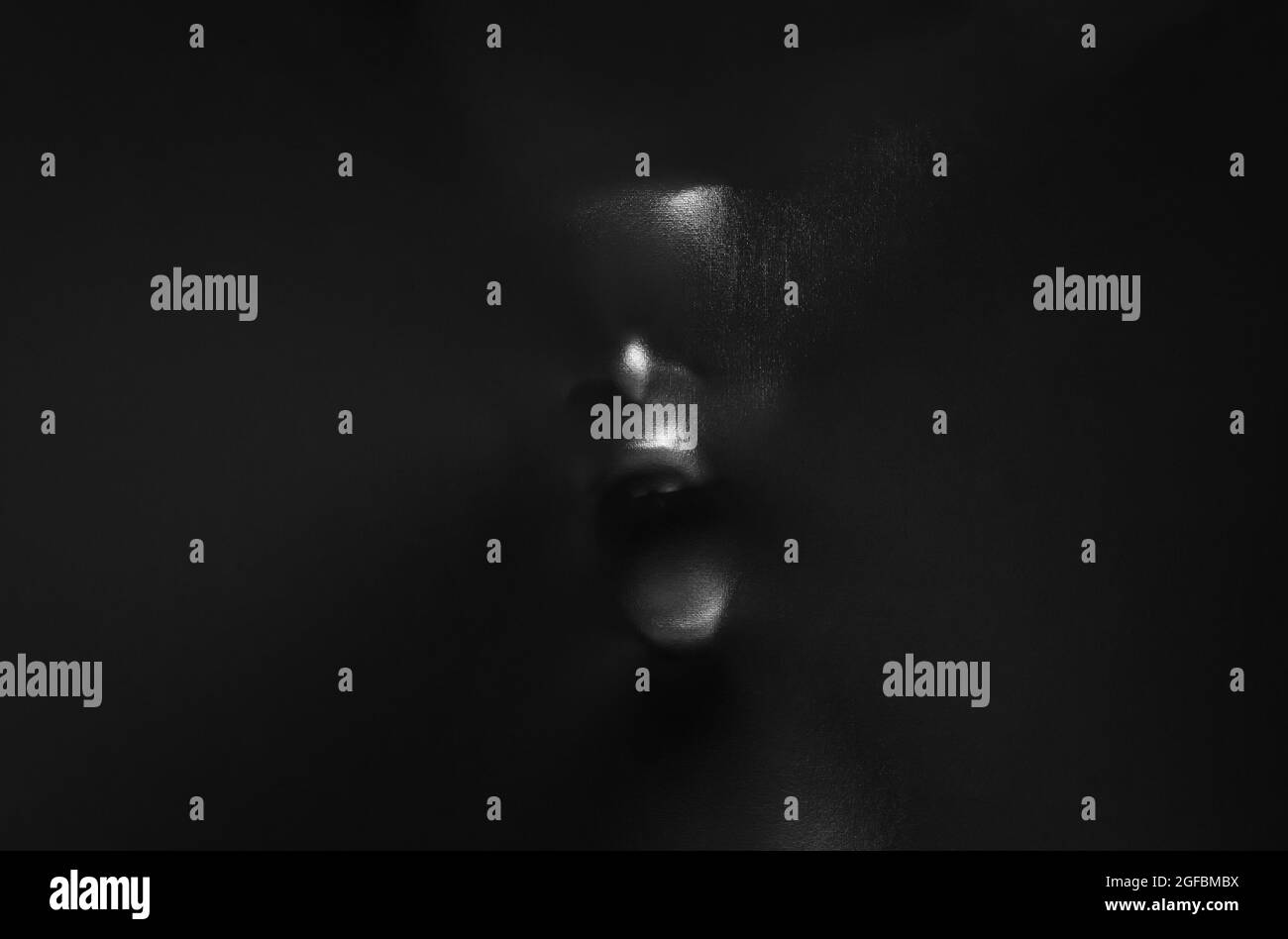 Screaming human face pressing through black fabric with shine and dark side for Halloween background concept. Stock Photo