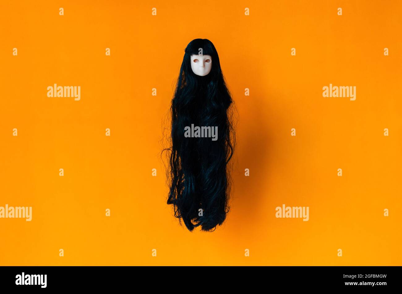 Long hair female ghost doll flying on orange background. Minimal Halloween scary concept. Stock Photo