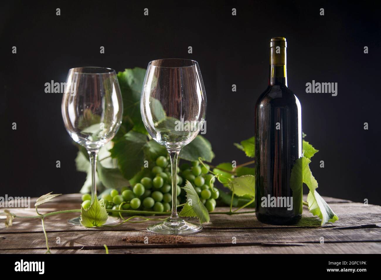 Glass of red wine with bottle and bunch of sour grapes on a black ...