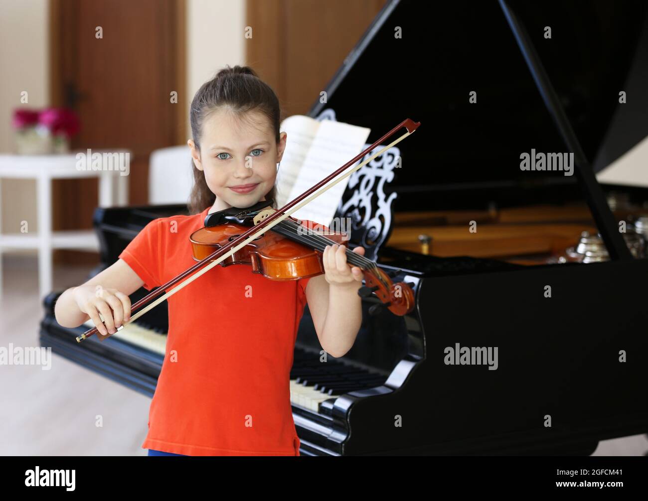 Little girl playing violin on piano background Stock Photo - Alamy