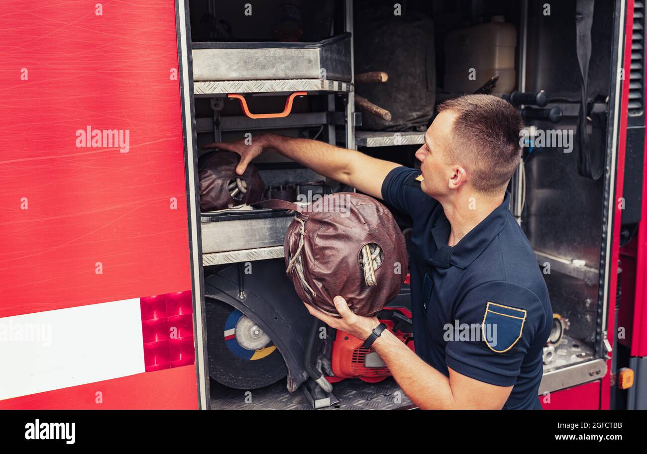 Fireman standing by fire truck, holding firefighting ropes for ...