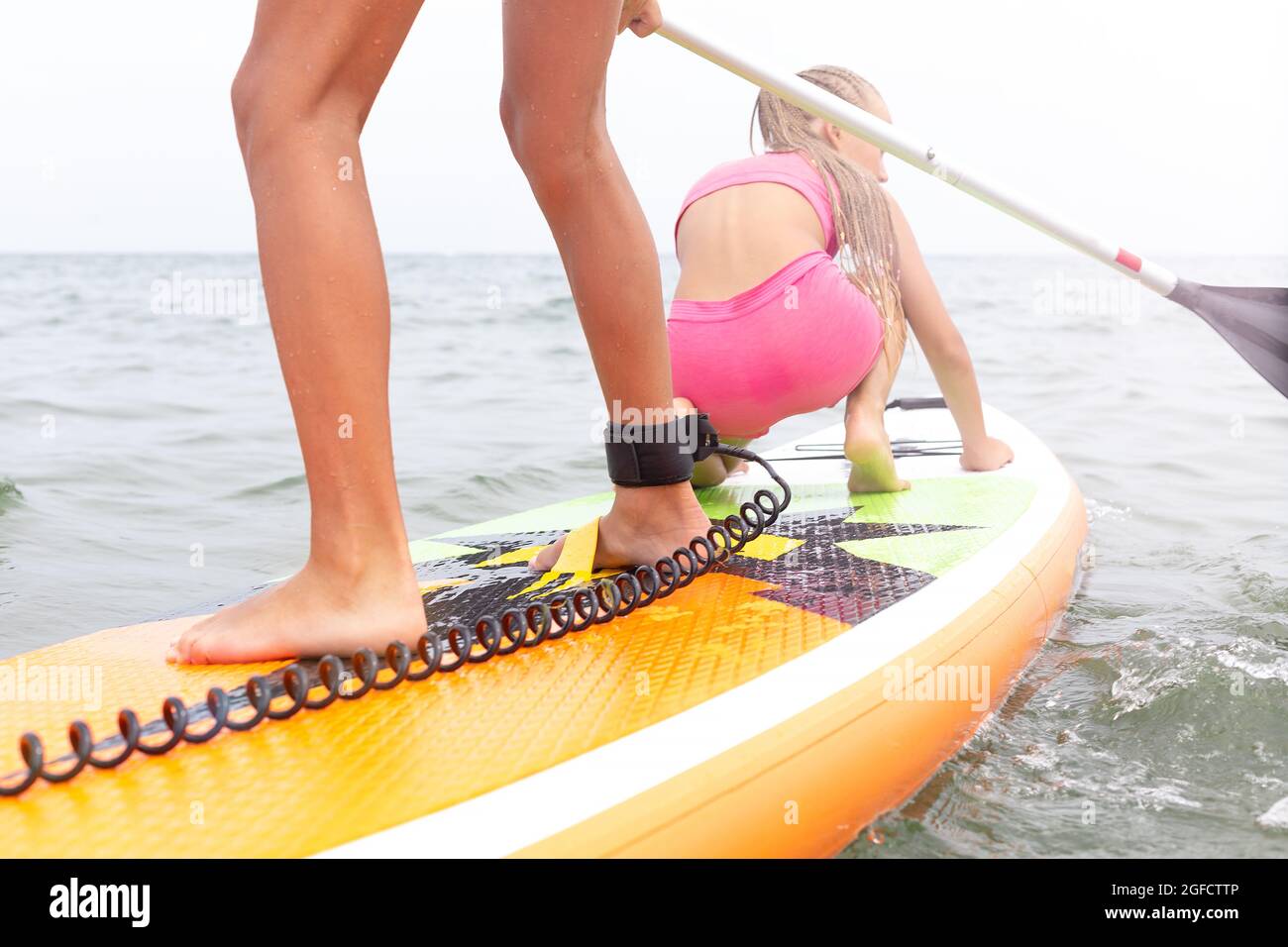 Stand up paddle board on the sea. Closeup of legs with a safety rope